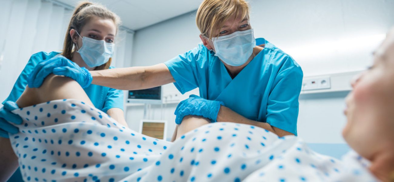 In the Hospital Professional Midwives Helping Spread Legs to Woman Pushes to Give Birth in Labor. Modern Maternity Ward with Professional Obstetricians.